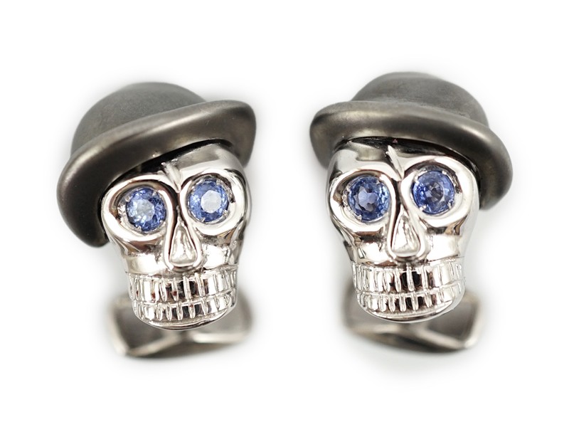 A modern pair of Longmire 18ct white gold, blackened rhodium and sapphire set novelty cufflinks, each modelled as a skull wearing a bowler hat